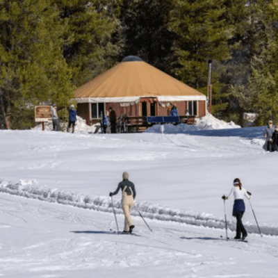 Two cross country skiiers going to a yurt with mountains in the background