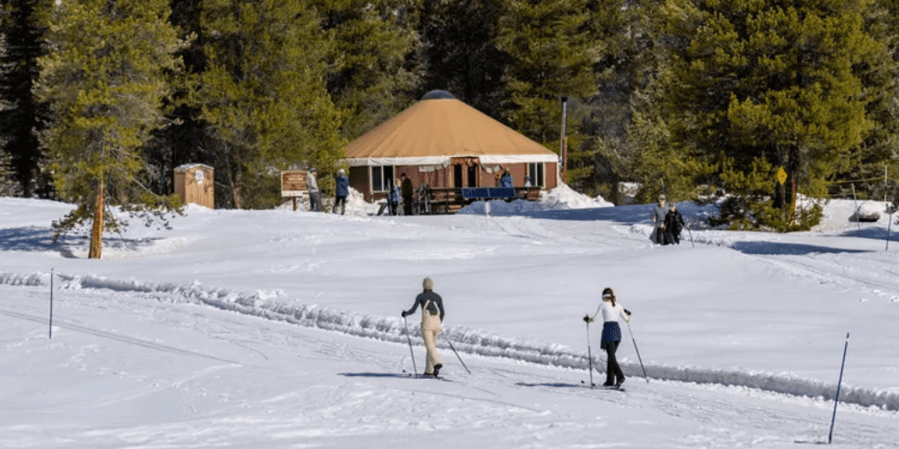 Two cross country skiiers going to a yurt with mountains in the background