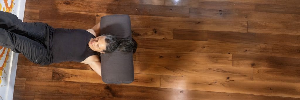 Alex Lambro in an inverted Kaiut pose with legs up the wall She is laying on a wood floor with soft lighting