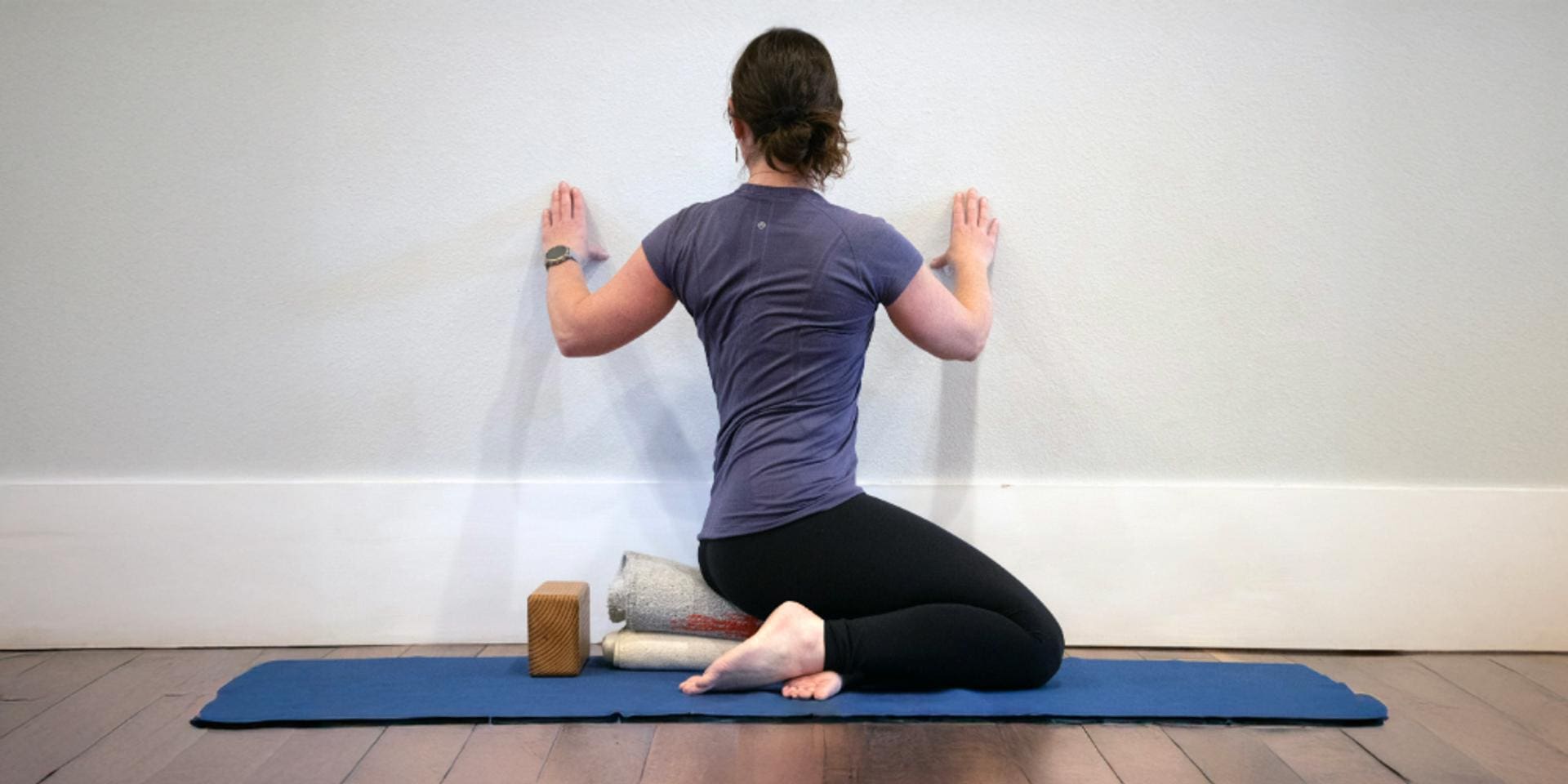 Iyengar yoga practitioner performing a supported seated twist with props against a wall, demonstrating spinal alignment and shoulder opening benefits of twisting poses.